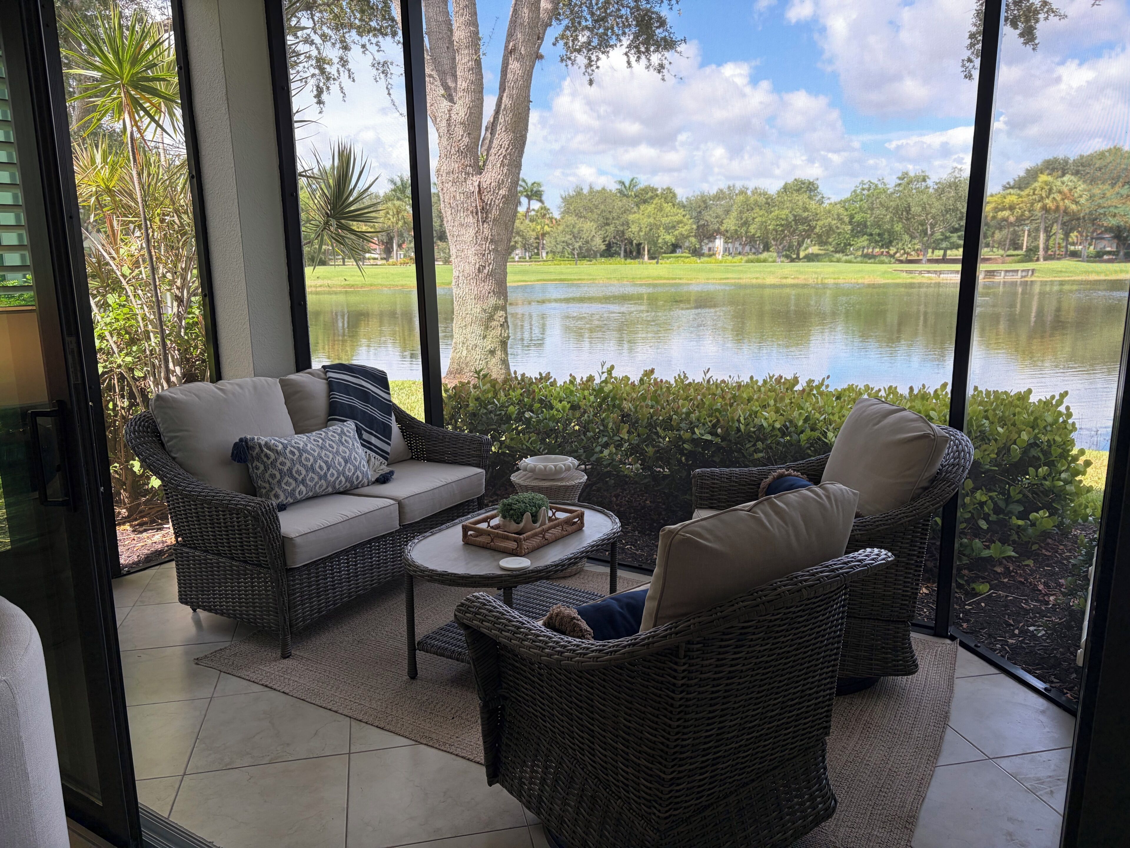 A room with wicker furniture, a view of a lake, and a golf course in the background.