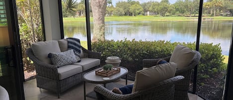 A room with wicker furniture, a view of a lake, and a golf course in the background.