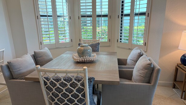 A dining area with a table and chairs, large windows with blinds, and a vase on the table. - Renovated Ravenna first floor townhome in exclusive Pelican Marsh. (Naples)