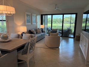 A modern living room with a sofa, chairs, a dining table, and a view of a lake through large glass doors. - Renovated Ravenna first floor townhome in exclusive Pelican Marsh. (Naples)
