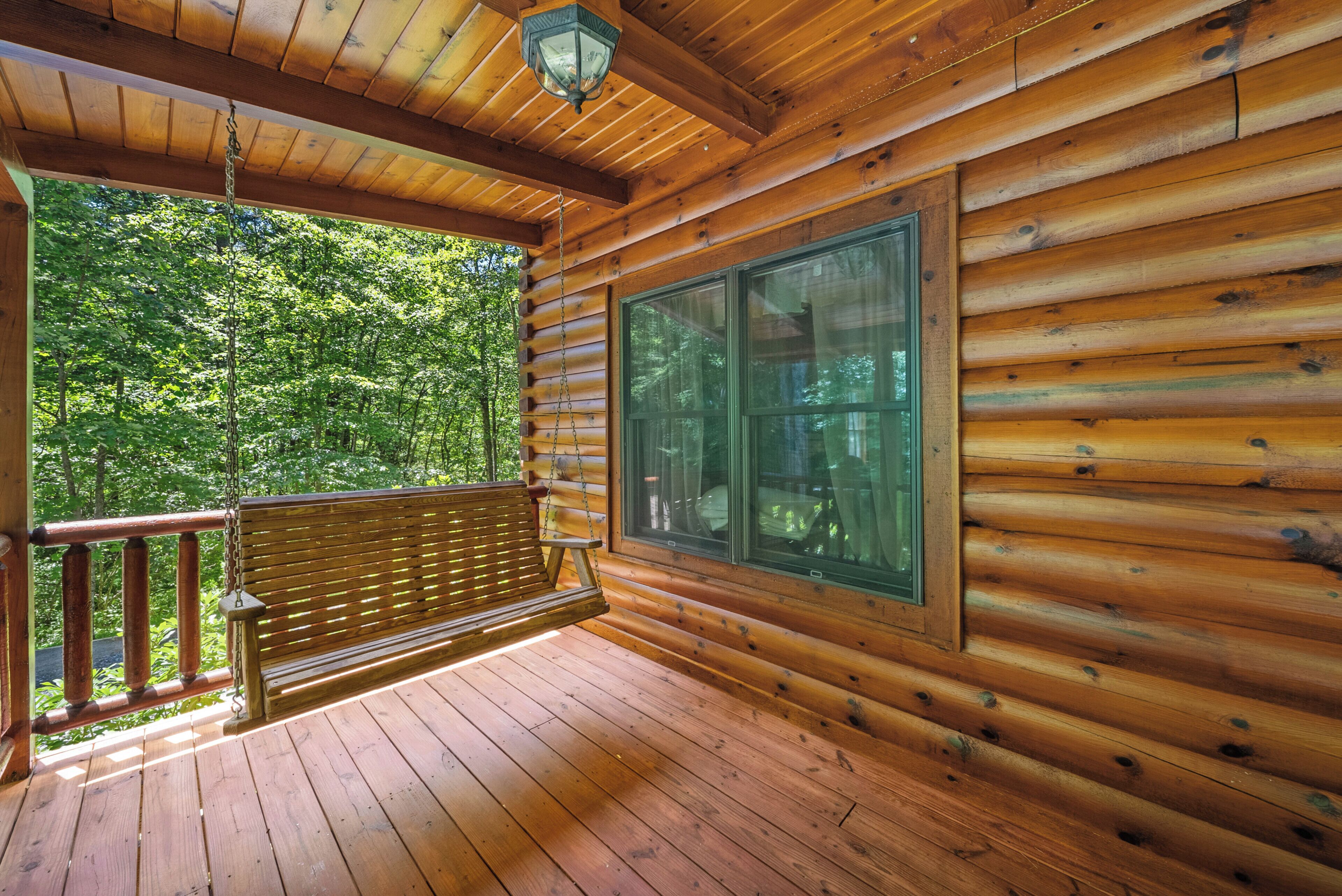 Une cabane en bois dotée d’une véranda, d’une balançoire et d’une grande fenêtre donnant sur une forêt.