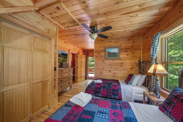 Una cabaña con dos camas, ventilador de techo, paredes de madera, un aparador y una ventana con vista.