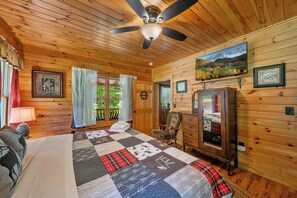 Ein Schlafzimmer einer Holzhütte mit Bett, Kommode, Stuhl und Deckenventilator.