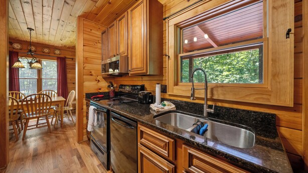 A wooden cabin interior with a kitchen, dining area, and large windows. - Classic Log Cabin with Hot Tub & Fire Pit (West Jefferson)