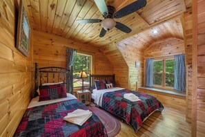Una cabaña con dos camas de madera, un ventilador de techo y una ventana con cortinas.