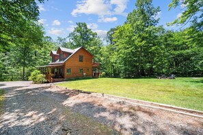Une cabane en rondins dotée d’un porche, entourée d’une pelouse bien entretenue et d’arbres denses.