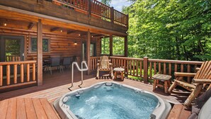A wooden deck with a hot tub, outdoor seating, and a view of the forest. - Classic Log Cabin with Hot Tub & Fire Pit (West Jefferson)