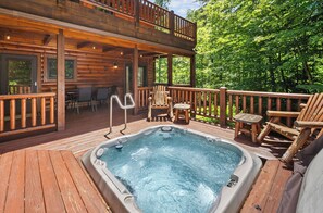 Eine Holzterrasse mit Whirlpool, Sitzgelegenheiten im Freien und Blick auf den Wald.