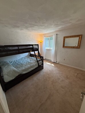 Une chambre avec un lit superposé, une fenêtre avec des rideaux, une lampe sur pied et un miroir au mur.