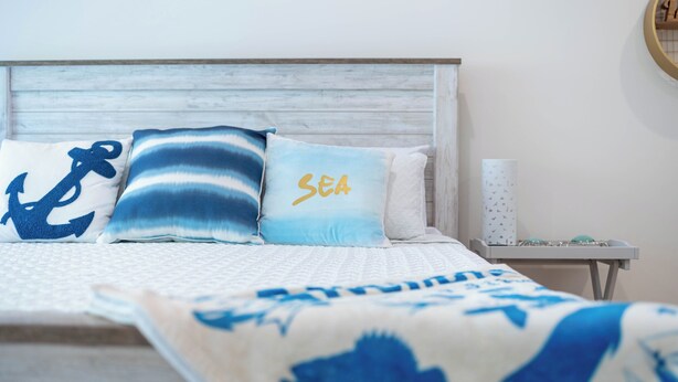 Un letto con copriletto bianco e blu a motivi decorativi, una testiera in legno e cuscini decorativi a tema nautico.