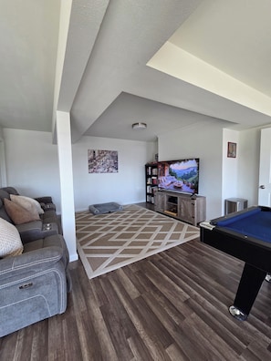 Una sala de estar con mesa de billar, sofá, televisión y estantería.