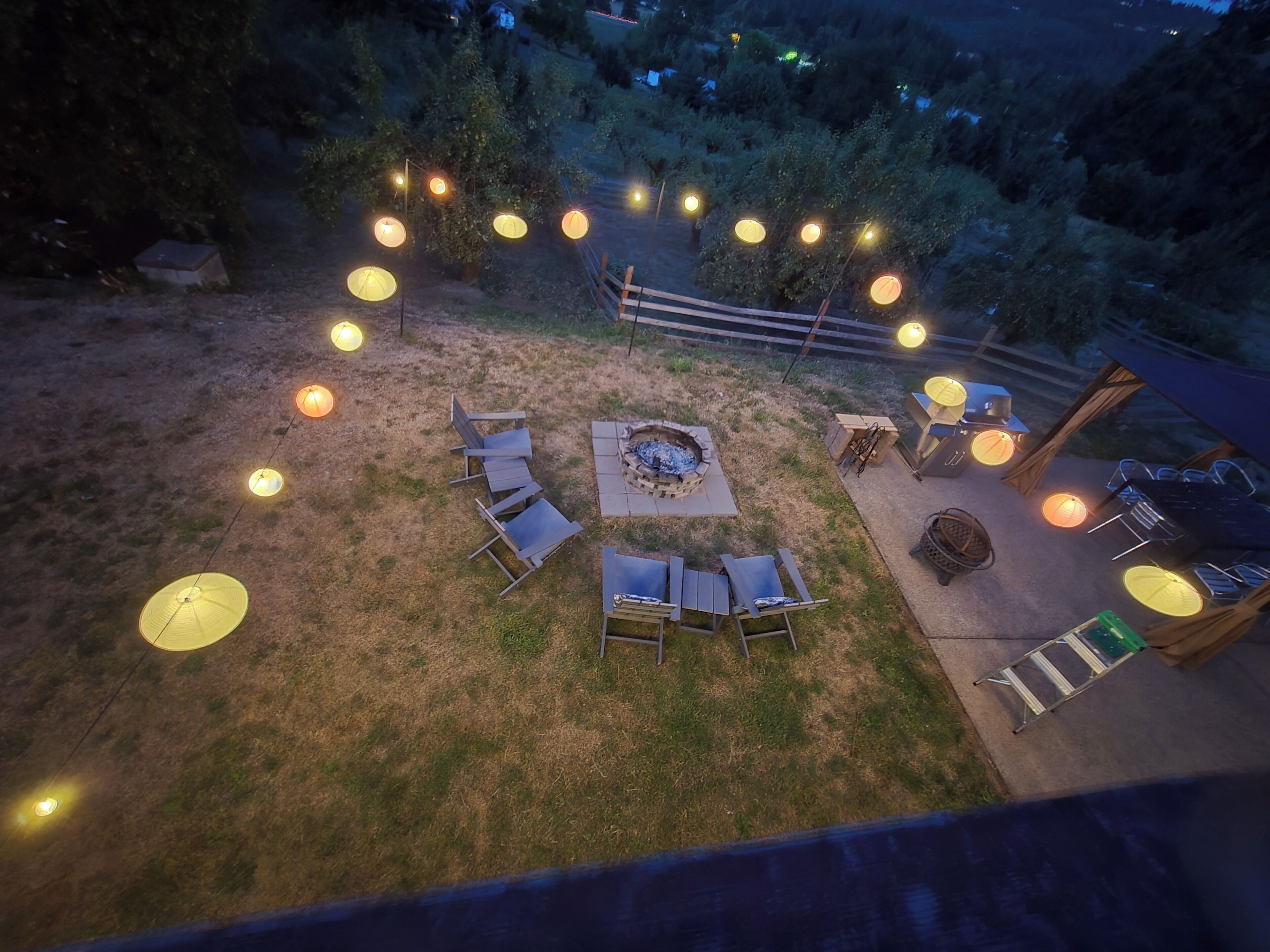 An outdoor seating area with a fire pit, surrounded by chairs and tables, and string lights.