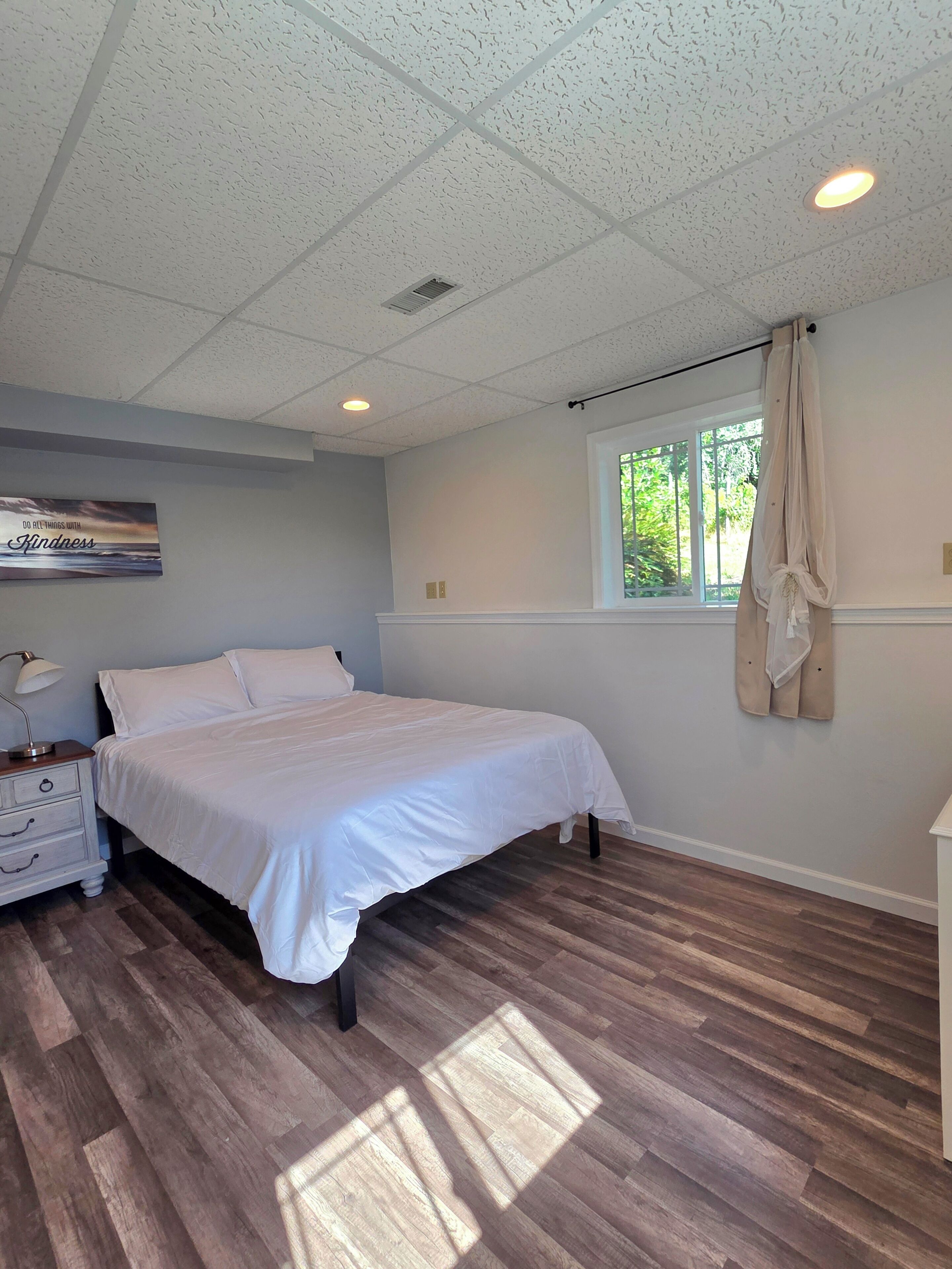 Un dormitorio con cama, mesita de noche y ventana con cortinas.