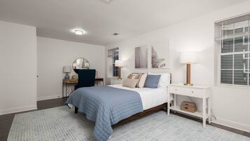 Ein Schlafzimmer mit einem Bett, Nachttischen, einem Schreibtisch, einem Sessel, einem Spiegel und Bildern an der Wand.