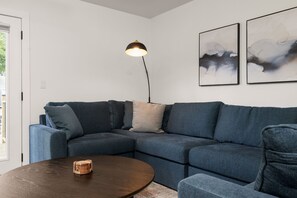 A modern living room with a sectional sofa, a round coffee table, a floor lamp, and abstract wall art. - Echoes on Eddy - Walk To Stadium & Outdoor Deck! (South Bend)
