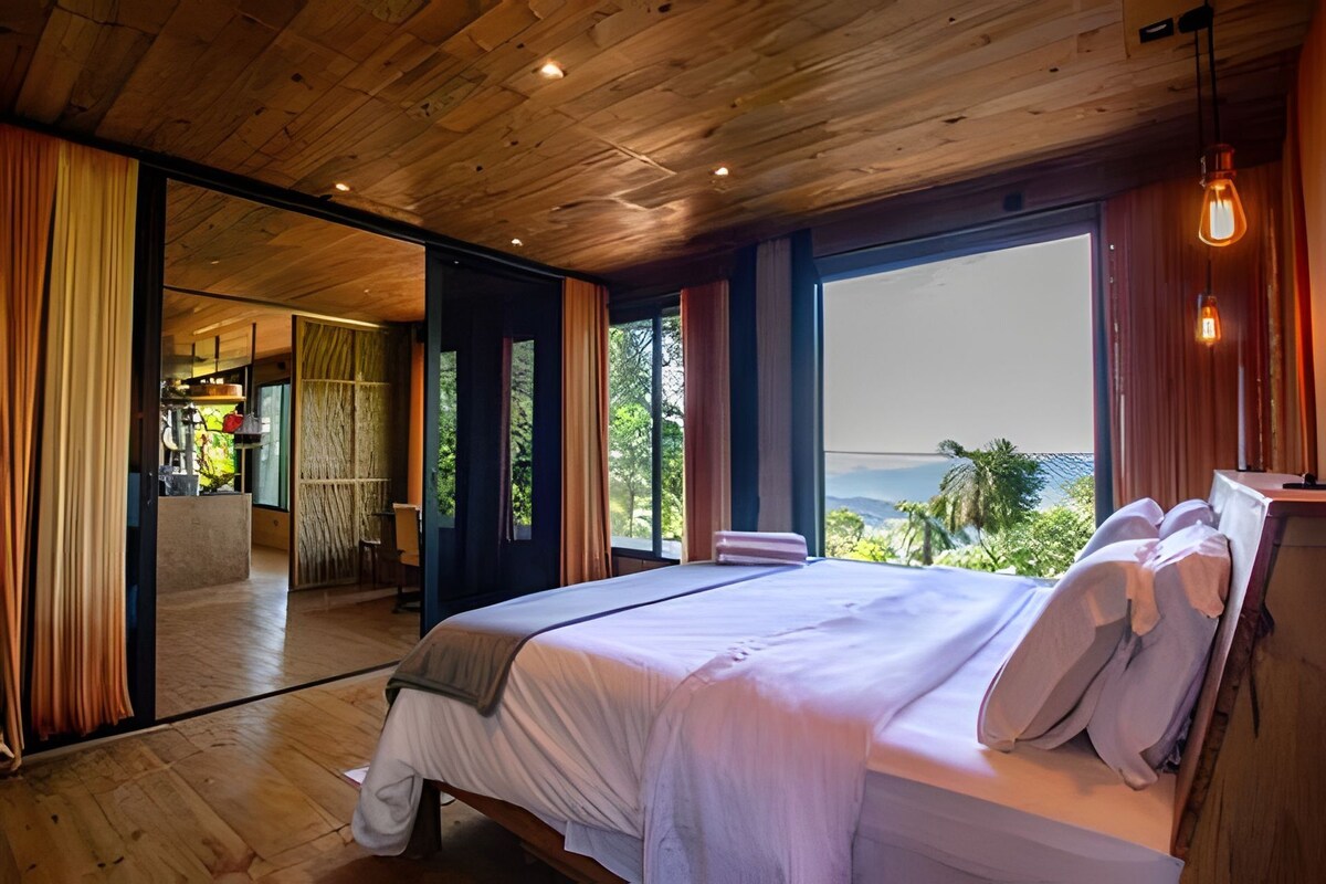 Ein Schlafzimmer mit einem großen Bett, Holzboden und Blick ins Freie.