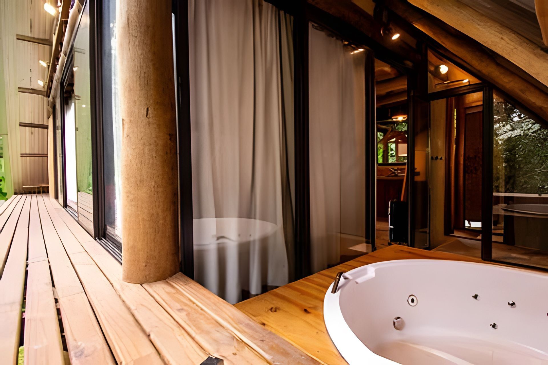 A wooden deck with a hot tub and a glass door leading to a room.