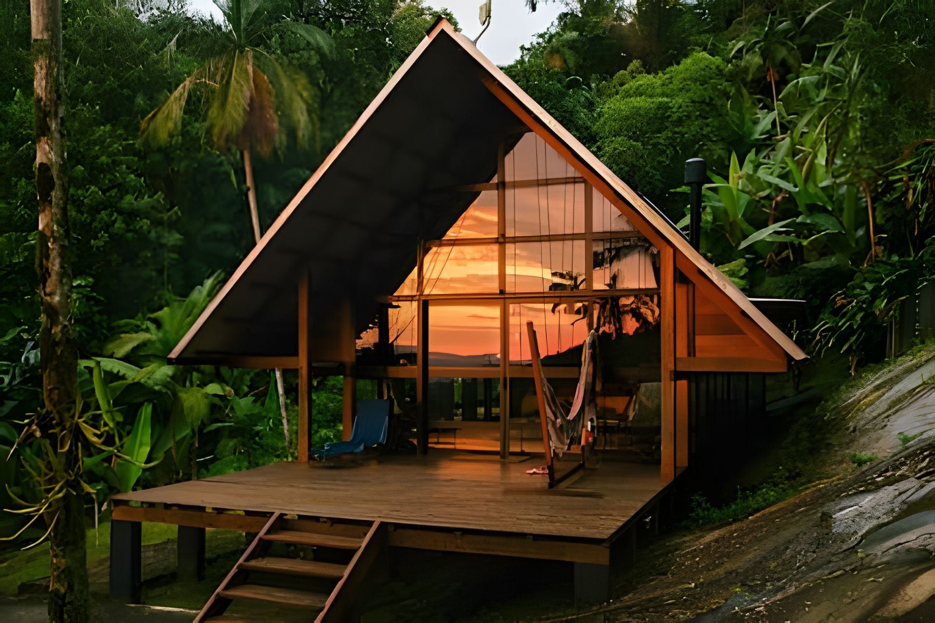 A wooden cabin with a sloped roof, surrounded by dense tropical vegetation.