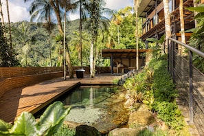 A wooden deck leading to a pool with a natural landscape in the background.