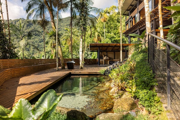 A wooden deck leading to a pool with a natural landscape in the background.