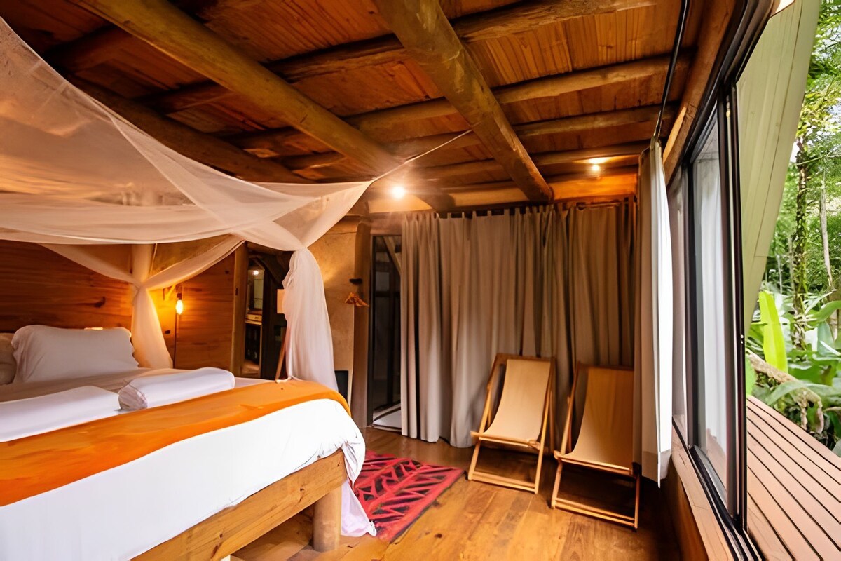 Ein Schlafzimmer einer Holzhütte mit einem Bett, einem Sessel und einem Fenster mit Blick auf Grünflächen.