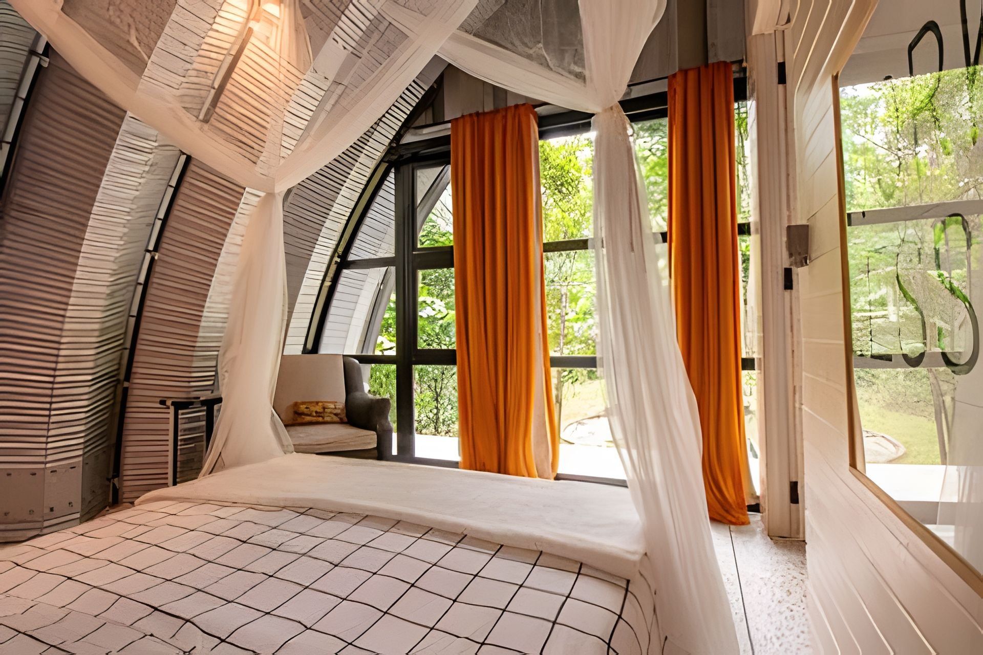 A bedroom with a curved ceiling, large windows with orange curtains, and a bed with a white and black checkered bedspread.