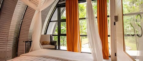 A bedroom with a curved ceiling, large windows with orange curtains, and a bed with a white and black checkered bedspread.