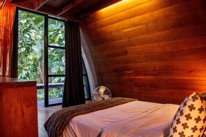 A bedroom with a large window, wooden walls, a bed, and a fan. - Aldeia Rizoma (Paraty)