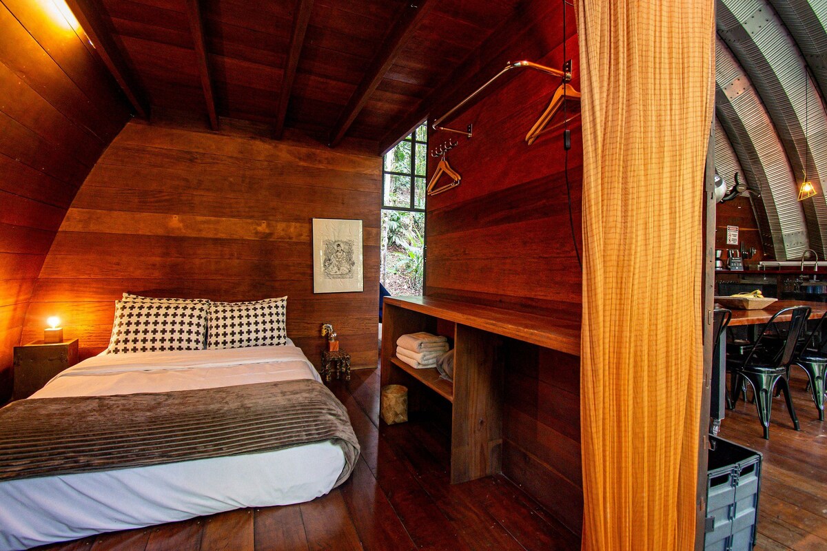 Ein gemütlicher, holzgetäfelter Raum mit einem Bett, einem kleinen Tisch und einer Bank.