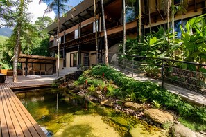 A modern building with a pool, surrounded by lush greenery and a wooden deck.