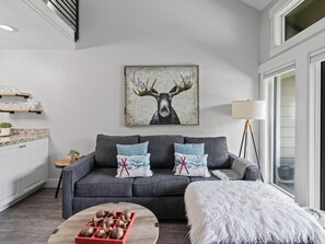 Ein modernes Wohnzimmer mit einem grauen Sofa, einem Couchtisch mit Holzkugeln, einem weißen, flauschigen Ottomanen, einem Elchgemälde an der Wand und einer Stehlampe.