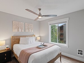 Ein Schlafzimmer mit Bett, Nachttischen, Deckenventilator, Fenster mit Blick und Wandbildern.