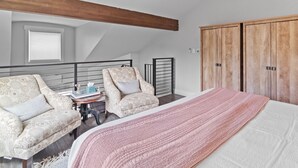 Une chambre à coucher avec un grand lit, deux fauteuils, une petite table avec un vase et une armoire en bois.
