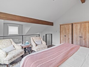 Ein Schlafzimmer mit einem großen Bett, zwei Sesseln, einem kleinen Tisch mit einer Vase und einem Holzschrank.