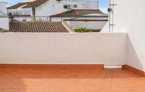 Eine Dachterrasse mit Terrakotta-Fliesen, einer weißen Wand und einem Blick auf angrenzende Gebäude mit Ziegeldächern.