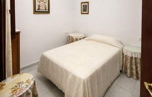 Ein Schlafzimmer mit einem Bett, zwei Nachttischen, einem kleinen runden Tisch und zwei gerahmten Bildern an der Wand.