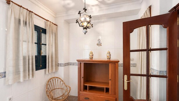 Una stanza con un armadio in legno, una sedia in vimini, una porta con pannelli di vetro e un lampadario.