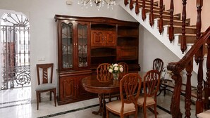 Un'area pranzo con tavolo e sedie in legno, un mobile con ante in vetro e una scala con ringhiere in legno.
