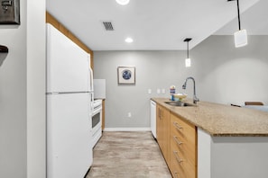 A compact kitchen with white appliances, a wooden cabinet, a sink, and a pendant light. - Resort Amenities-Ground Floor-Walk To Baytowne Wharf-E5109 (Miramar Beach)