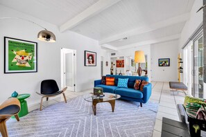 A modern living room with a blue sofa, a glass coffee table, and a green stool. - Meiselman Palms - A Ryson Property (Palm Springs)