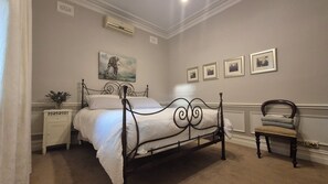 Ein Schlafzimmer mit einem Himmelbett, einem Nachttisch mit einer Vase, einem Sessel und gerahmten Bildern an der Wand.