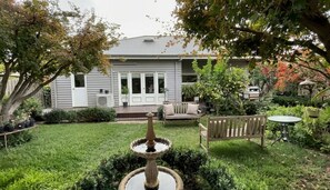 Una casa con porche delantero, jardín con fuente y mobiliario exterior.