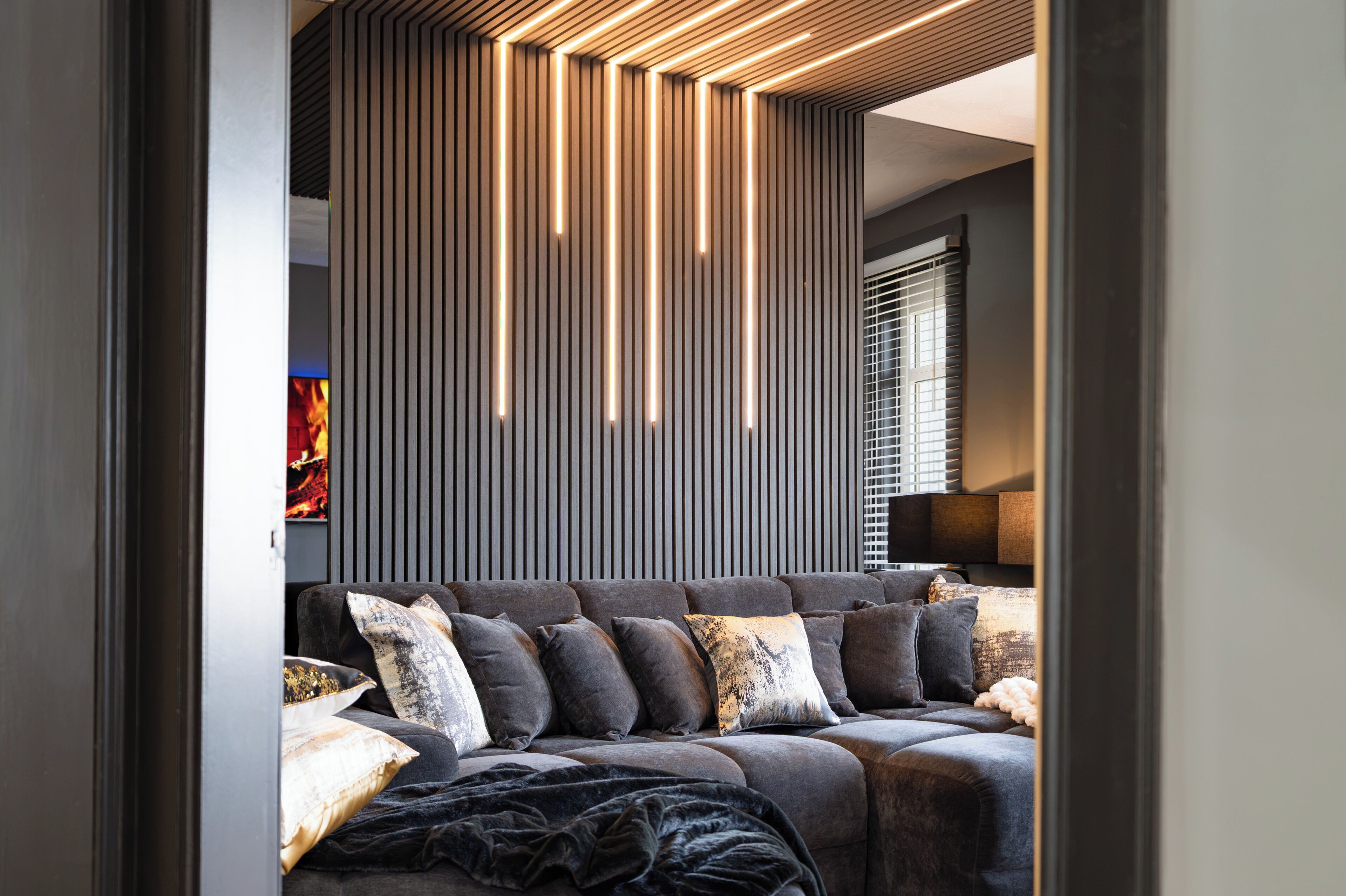 A modern living room with a sofa, pillows, and a wall with vertical lines and lighting.