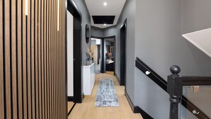 Un pasillo moderno con un panel de madera, barandilla negra y alfombra gris que conduce a una habitación con cama y escritorio.