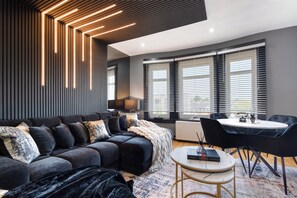 A modern living room with a sectional sofa, a round coffee table, and a dining area with a small table and chairs. - The Glasgow Pad (Glasgow)