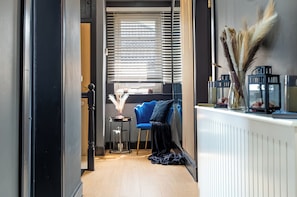 Un couloir étroit avec une chaise bleue, une petite table ornée de quelques objets décoratifs et un radiateur.
