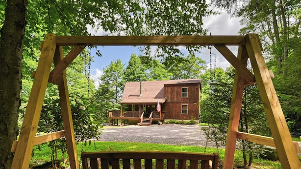 A wooden swing set overlooking a rustic house with a porch and a gravel driveway. - Charming 4BR Cabin - HOT TUB - Mountain View (Oakland)