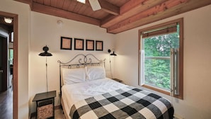 A bedroom with a bed, a ceiling fan, a window with a view of trees, and framed pictures on the wall. - Charming 4BR Cabin - HOT TUB - Mountain View (Oakland)