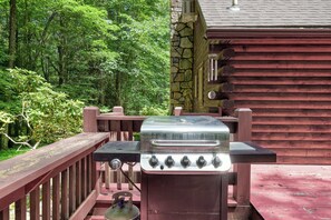 Ein Grill mit Gasflasche, eine Holzterrasse und eine Steinmauer.