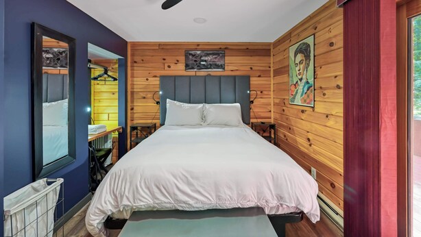 Una camera da letto con un letto, una ventola a soffitto, pareti in legno, una finestra e una porta.